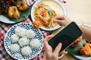 Kadın akıllı telefonuyla Isan yemeklerini çekiyor. Gıda blogcusu için alanı kopyala ve modelle.