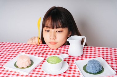 Sarı kaşık tutan genç Asyalı kadın pembe masadaki tatlı pirinç kaselerine bakıyor..