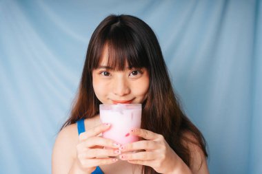 Elinde bir bardak pembe milkshake tutan Asyalı genç kadının portresi..