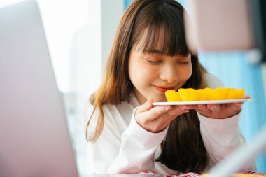 Genç Asyalı siyah saçlı kadın, akıllı telefon kamerasının önünde Tayland tatlısı yemek eleştirisi yapıyor..