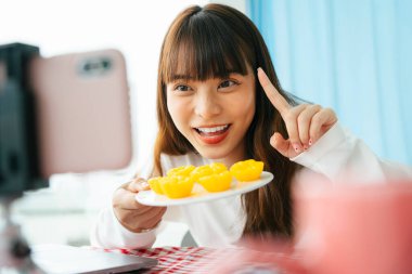 Genç Asyalı siyah saçlı kadın, akıllı telefon kamerasının önünde Tayland tatlısı yemek eleştirisi yapıyor..