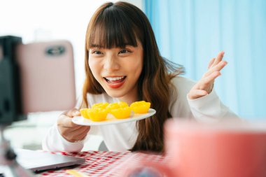 Genç Asyalı siyah saçlı kadın, akıllı telefon kamerasının önünde Tayland tatlısı yemek eleştirisi yapıyor..