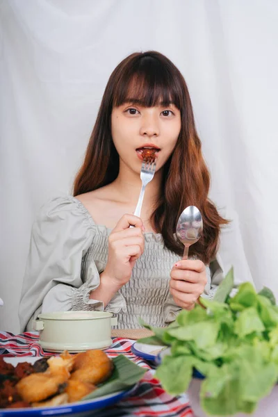 Evde çatal ve kaşıkla Isan yemeği yiyen Asyalı kadın portresi.