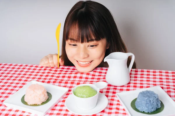 Sarı kaşık tutan genç Asyalı kadın pembe masadaki tatlı pirinç kaselerine bakıyor..