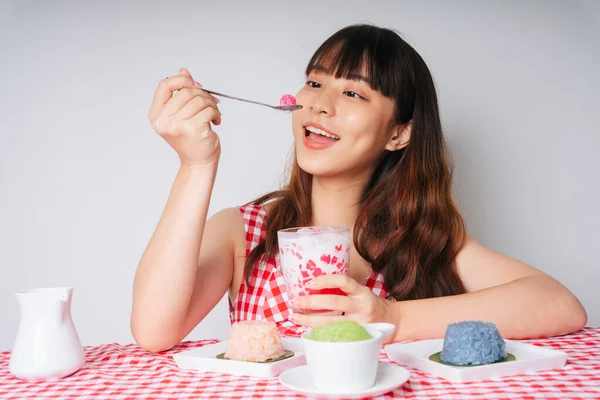 Genç Asyalı kadın kaşıkla su kestane tatlısı yiyor..