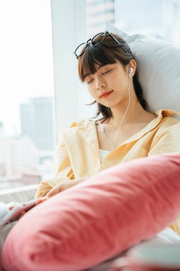 Uyuyan genç Asyalı siyah saçlı kadın. Yatakta kulaklıkla müzik dinliyor..