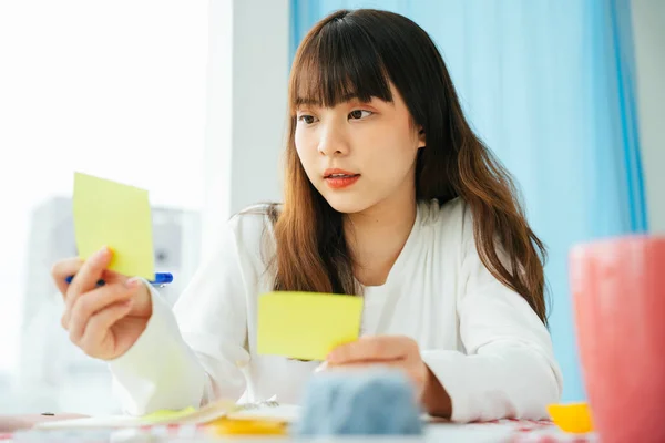 Young asian dark hair woman writing and planning works on sticky note paper.