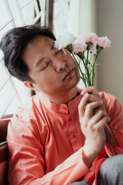 Pencere kenarında oturan Asyalı eşcinsel çiçekleri elinde tutuyor. Asya normu onu kendisi olmaktan alıkoyamaz..
