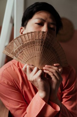 Siyah saçlı geyin dikey görüntüsü yüzünü ahşap pervaneyle kaplıyor..