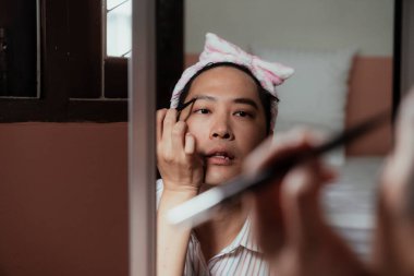 Kaşını çizen pembe bantlı Asyalı gay aynasındaki yansıma..