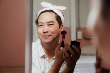 Makyajını yaparken Asyalı mutlu gay aynasından yansıyor..