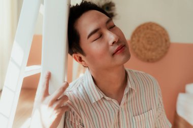 Mutlu Asyalı gay ranzanın direğine eğiliyor gözleri kapalı.