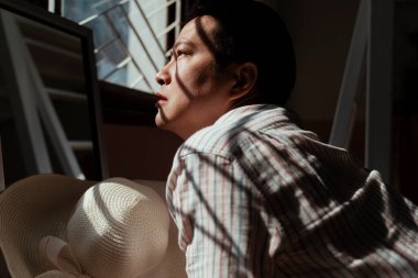 Asyalı gey güneşlenmek istiyor, o da pencerenin önünde güneş ışığında oturuyor..