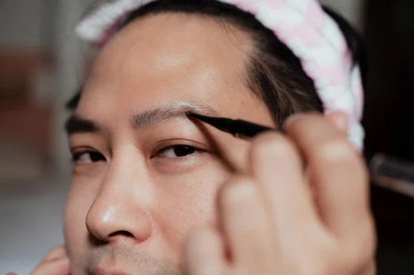 Cropped image of asian gay\'s eyebrow while he draw it during makeup.