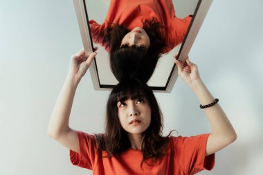 Yansımasını baş aşağı yapan aynayı kafasında tutan bir kız..