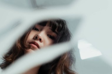 Yerdeki kırık ayna uzun kıvırcık saçlı kızı yansıtıyor..