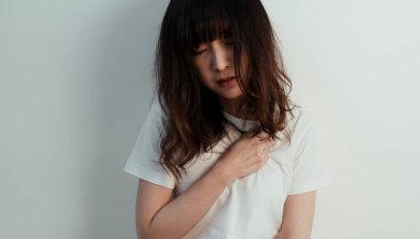 Kıvırcık uzun saçlı kız beyaz duvarda otururken kalbi ağrıyor..