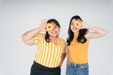 Sağlıksız çörek tutan iki Asyalı tombul ve zayıf kadın beyaz arka planda izole edilmiş..