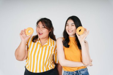 Sağlıksız çörek tutan iki Asyalı tombul ve zayıf kadın beyaz arka planda izole edilmiş..