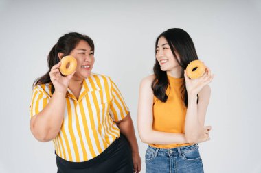 Sağlıksız çörek tutan iki Asyalı tombul ve zayıf kadın beyaz arka planda izole edilmiş..