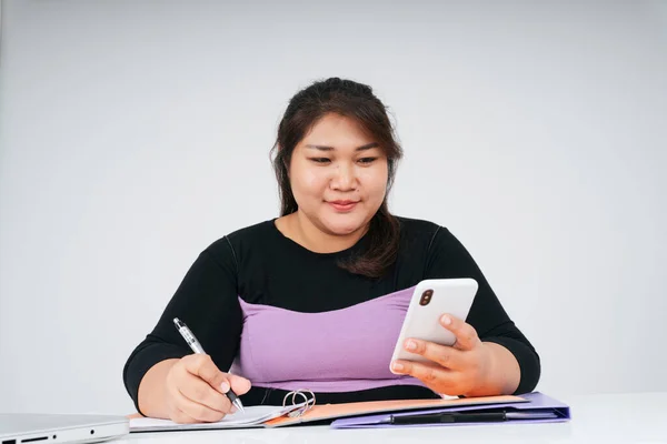 Asian chubby business woman working at desk holding smartphone at white background.