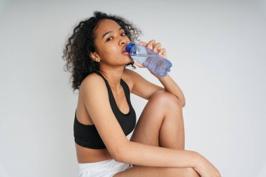 Karışık ırk Afrikalı ve Taylandlı kadın beyaz arka planda şişeden su içiyorlar..