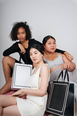 Asyalı ve Afrikalı üç farklı kadının toplu portresi, ellerinde alışveriş torbaları var..