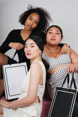 Asyalı ve Afrikalı üç farklı kadının toplu portresi, ellerinde alışveriş torbaları var..