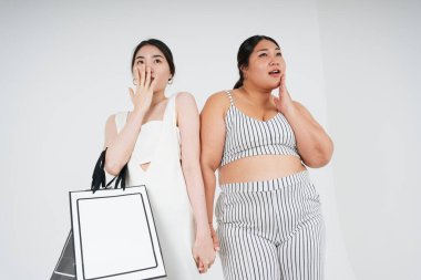 Asyalı lezbiyen çift beyaz arka planda alışverişe giderken el ele tutuşuyorlar.