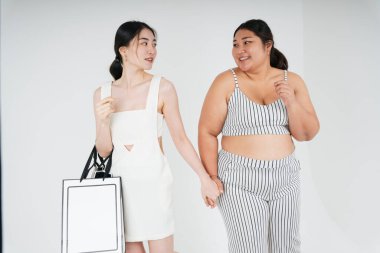 Asyalı lezbiyen çift beyaz arka planda alışverişe giderken el ele tutuşuyorlar.