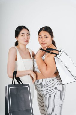 Asyalı kadınlar beyaz arka planda birlikte alışveriş yapmak için el ele tutuşuyorlar..