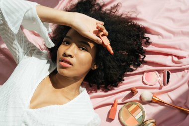 Üst Manzara - Afrika kıvırcık saç stili pembe kumaşın üzerinde ruj tutuyordu.