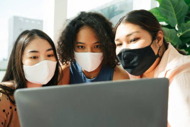 Çeşitlilik toplumu konsepti. Maske takan Asyalı ve Afrikalı kadınlar dizüstü bilgisayarla canlı yayın yapıyorlar..