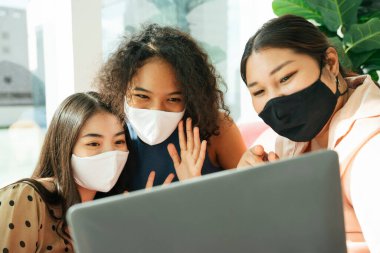 Maske takan bir grup kadın evde bilgisayar laptopuyla dolaşıyorlar..