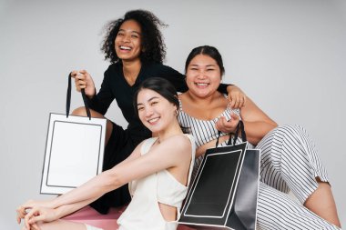 Asyalı ve Afrikalı üç farklı kadının grup portresi beyaz arka planda taklit etmek için alışveriş torbaları tutuyor..