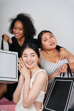 Asyalı ve Afrikalı üç farklı kadının grup portresi beyaz arka planda taklit etmek için alışveriş torbaları tutuyor..