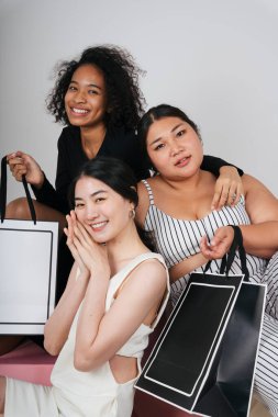 Asyalı ve Afrikalı üç farklı kadının grup portresi beyaz arka planda taklit etmek için alışveriş torbaları tutuyor..