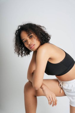 Afrikalı sporcu kadın beyaz arka planda siyah spor sutyenli kıvırcık saçlı..