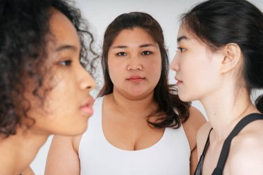 Beyaz spor sutyen giyen Asyalı şişman kadın portresi. Beyaz arka planda Asyalı ve Afrikalı insanların yüzü var. Çeşitlilik kavramı.