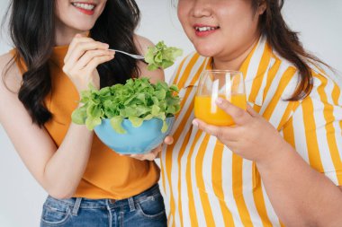 Neşeli Asyalı kadınlar sağlıklı salata kasesi yemeyi ve portakal suyunu beyaz arka planda izole etmeyi severler..