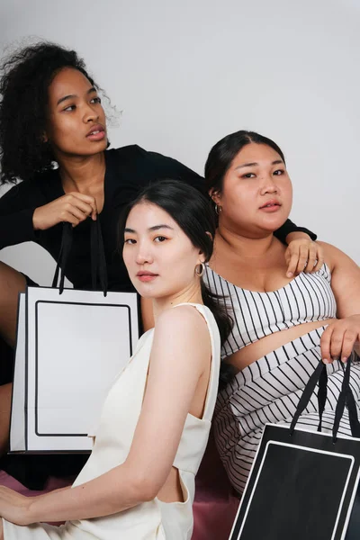 Asyalı ve Afrikalı üç farklı kadının toplu portresi, ellerinde alışveriş torbaları var..