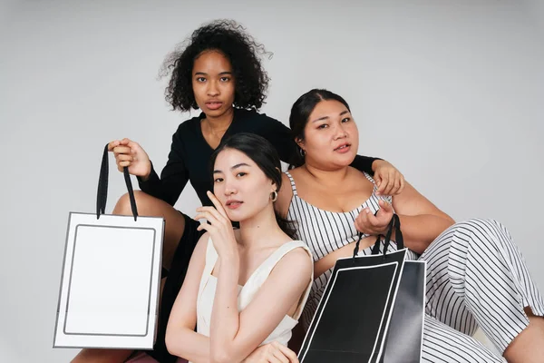Group portrait of three diverse women with asian and african holding shopping bags for mock up.