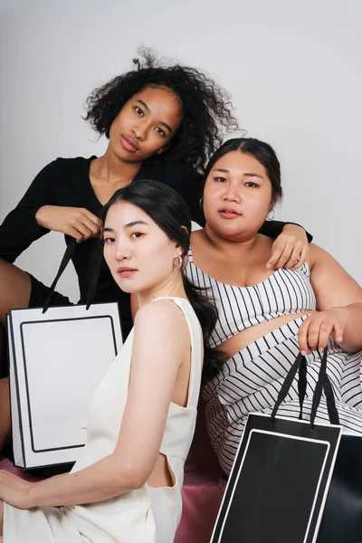 Asyalı ve Afrikalı üç farklı kadının toplu portresi, ellerinde alışveriş torbaları var..