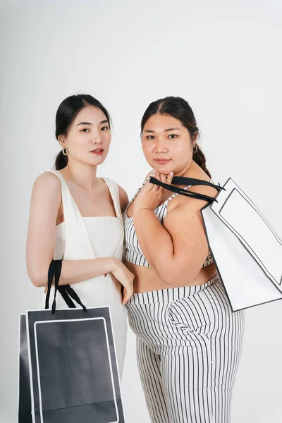 Asyalı kadınlar beyaz arka planda birlikte alışveriş yapmak için el ele tutuşuyorlar..