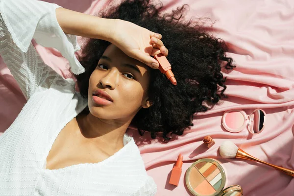 Üst Manzara - Afrika kıvırcık saç stili pembe kumaşın üzerinde ruj tutuyordu.
