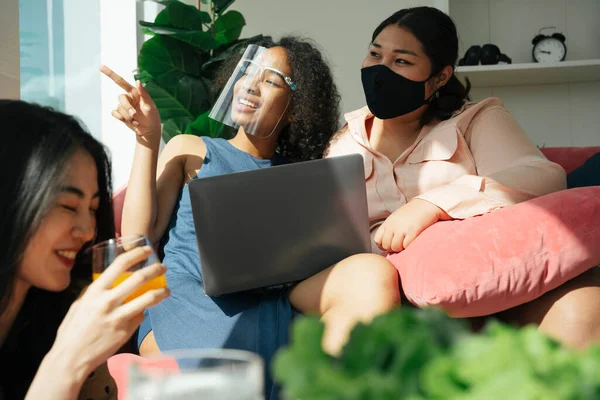Çeşitlilik toplumu konsepti. Asyalı ve Afrikalı kadınlar evde dizüstü bilgisayar kullanarak yüz maskesi takıyorlar..