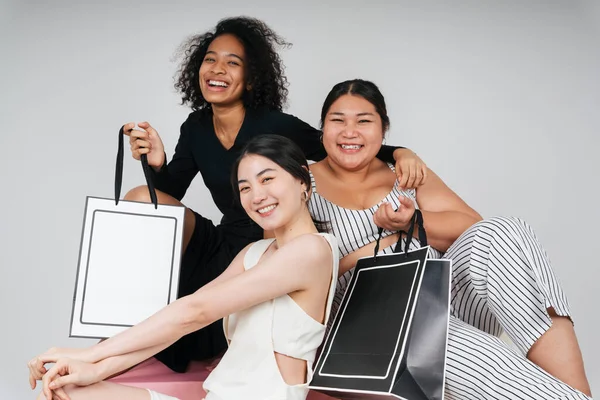 Asyalı ve Afrikalı üç farklı kadının grup portresi beyaz arka planda taklit etmek için alışveriş torbaları tutuyor..