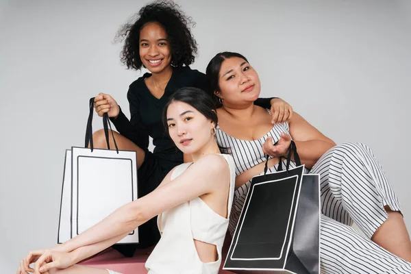 Group portrait of three diverse women with asian and african holding shopping bags for mock up on white background.