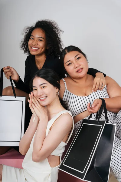 Asyalı ve Afrikalı üç farklı kadının grup portresi beyaz arka planda taklit etmek için alışveriş torbaları tutuyor..
