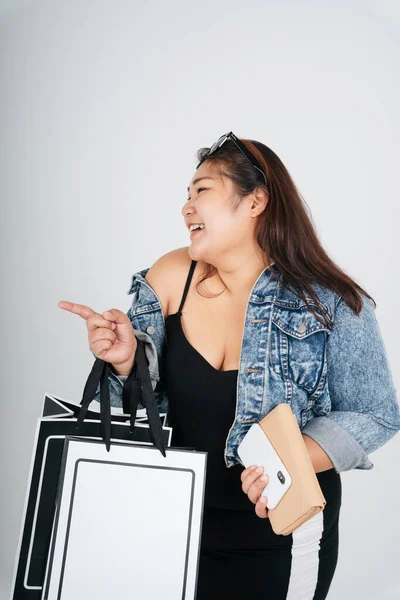 Portrait of fat woman in black dress and jeans jacket holding shopping paper bags isolate over white background.